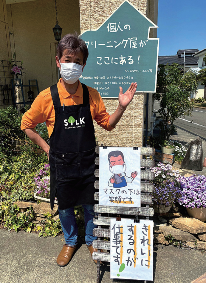 店頭のポスターとマスクの下で笑顔を作る石井さん