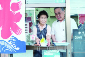 店は檜原街道沿いにある。ウクライナかき氷を手渡す理男店主（右）と幸子さん